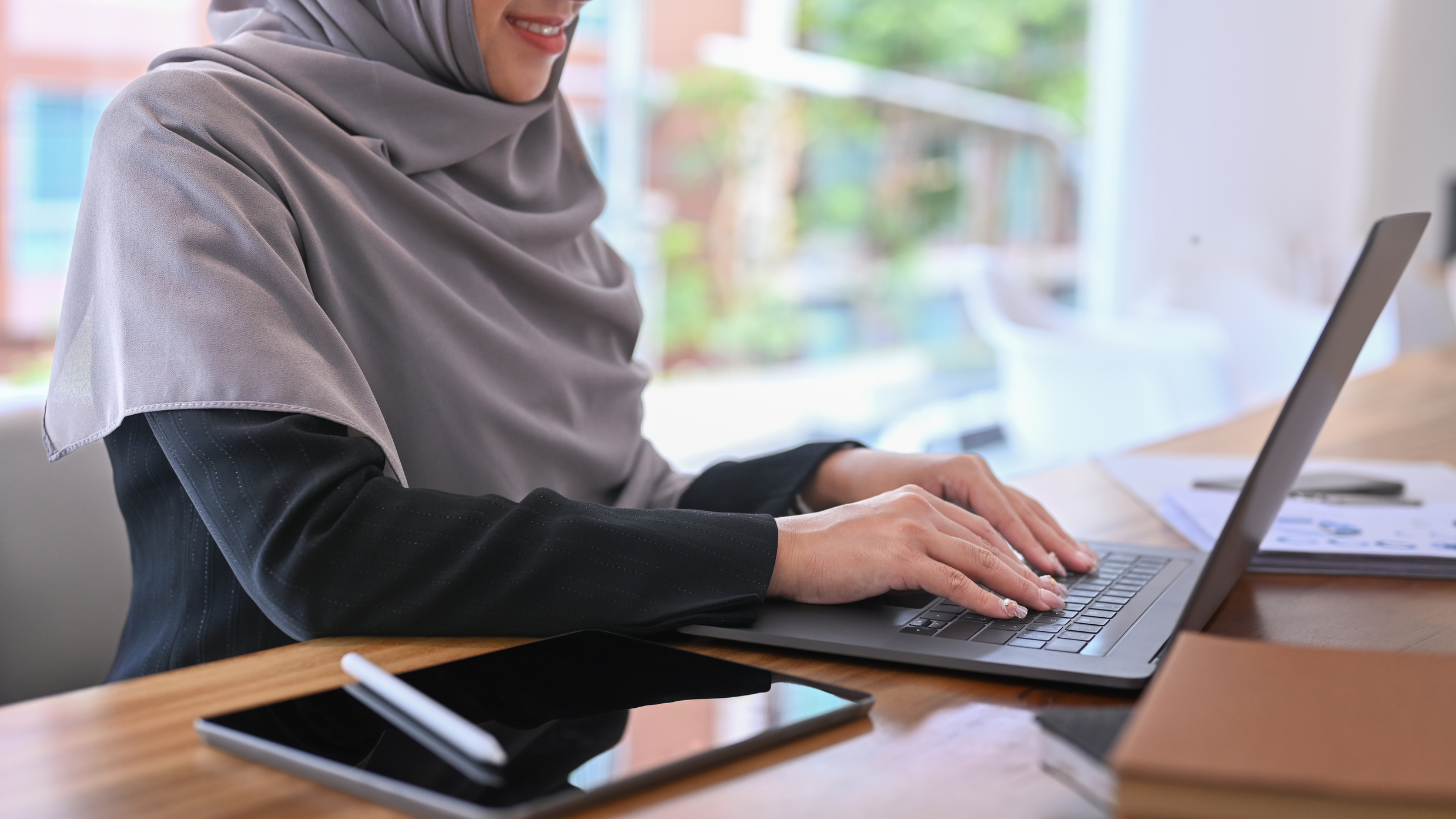 Smiling female muslim office worker using laptop computer wh