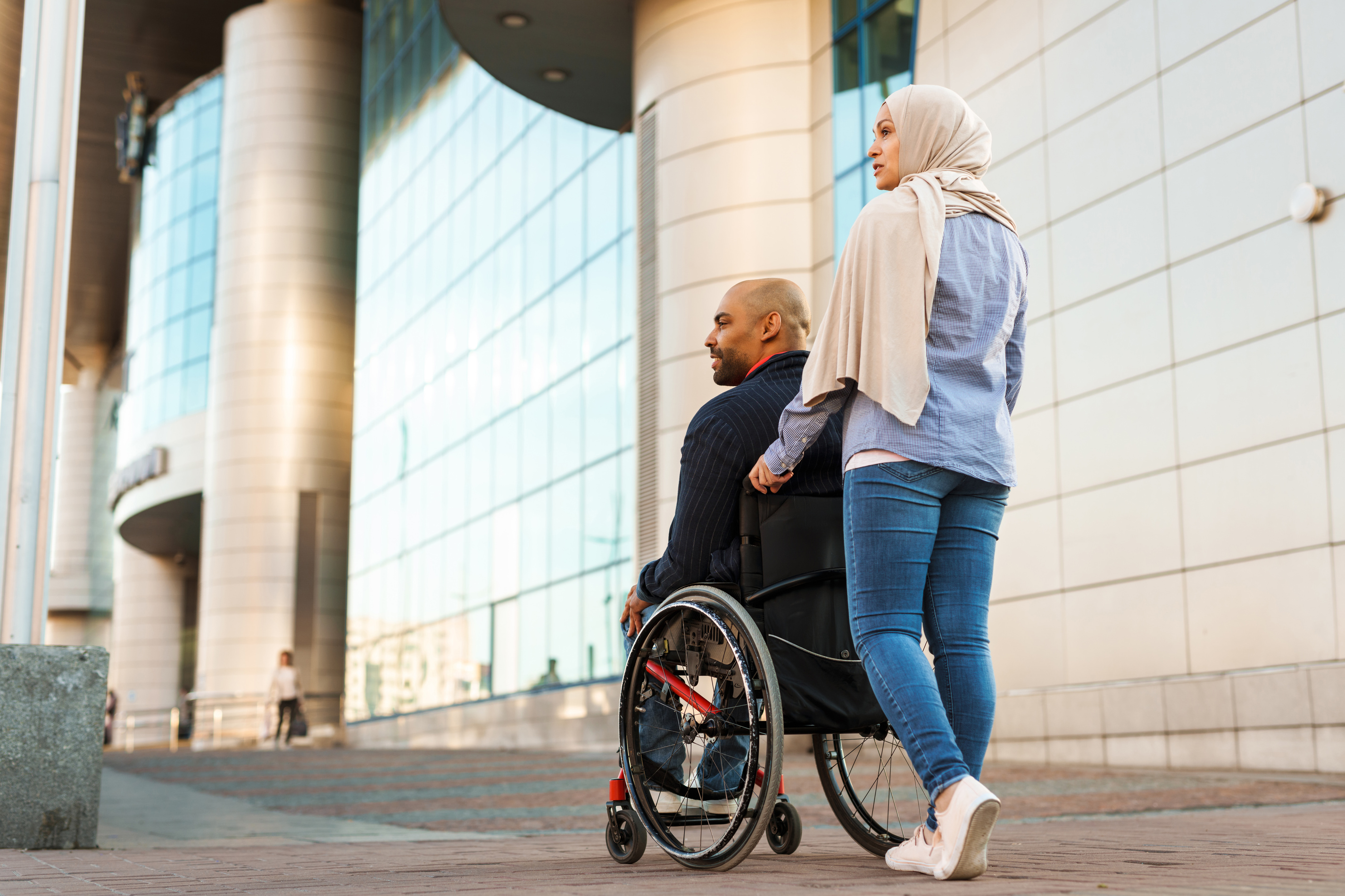 Muslim Woman and Man in Wheelchair Walking Together Outdoors